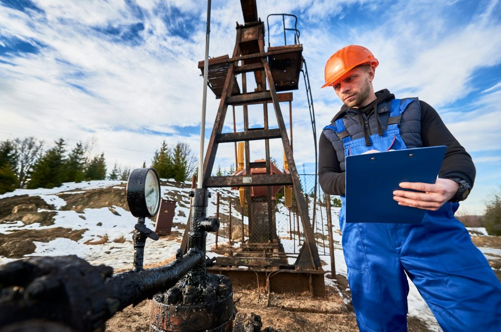 Petroleum engineer inspecting pump jack in oil field.